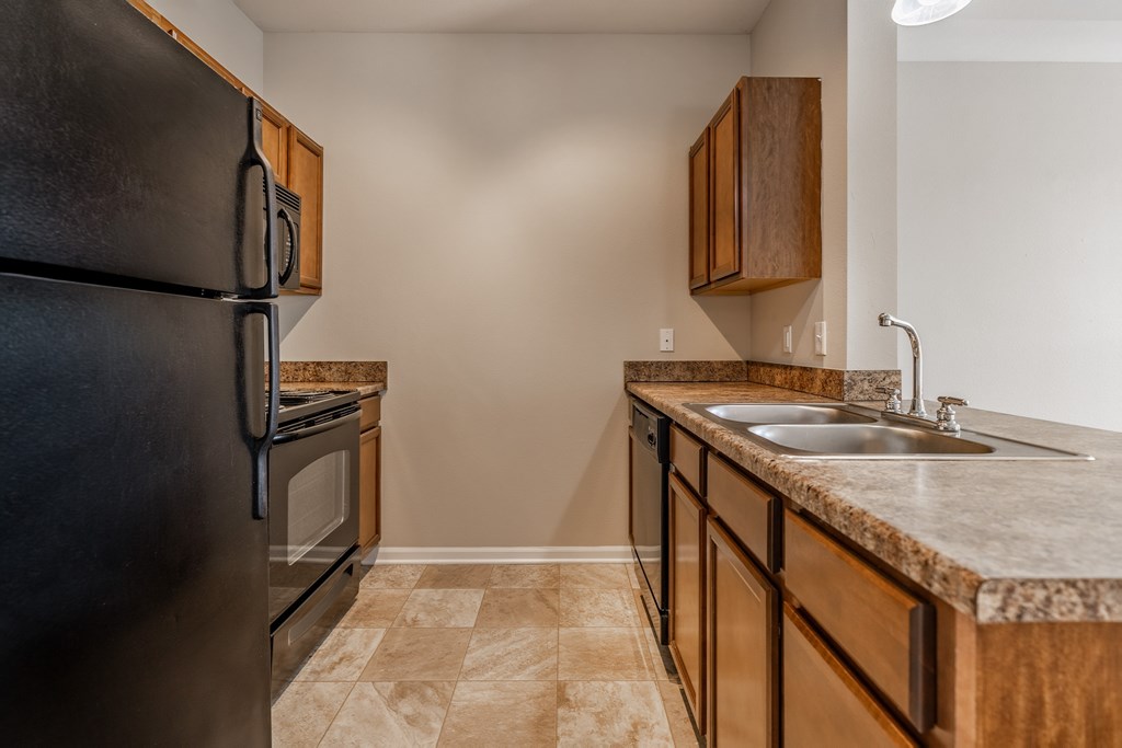 A kitchen with a black refrigerator and brown cabinets