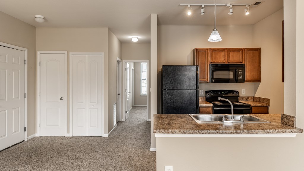 A kitchen with a black fridge and microwave, brown cabinets, and a brown countertop
