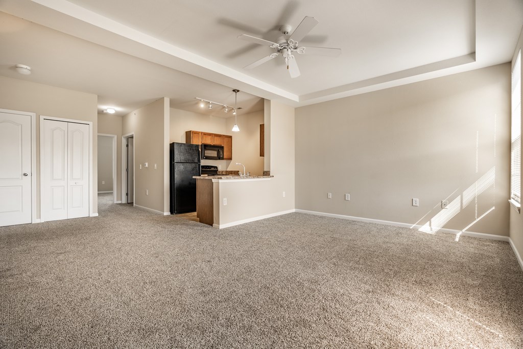 A spacious living room with a ceiling fan and carpeted floor