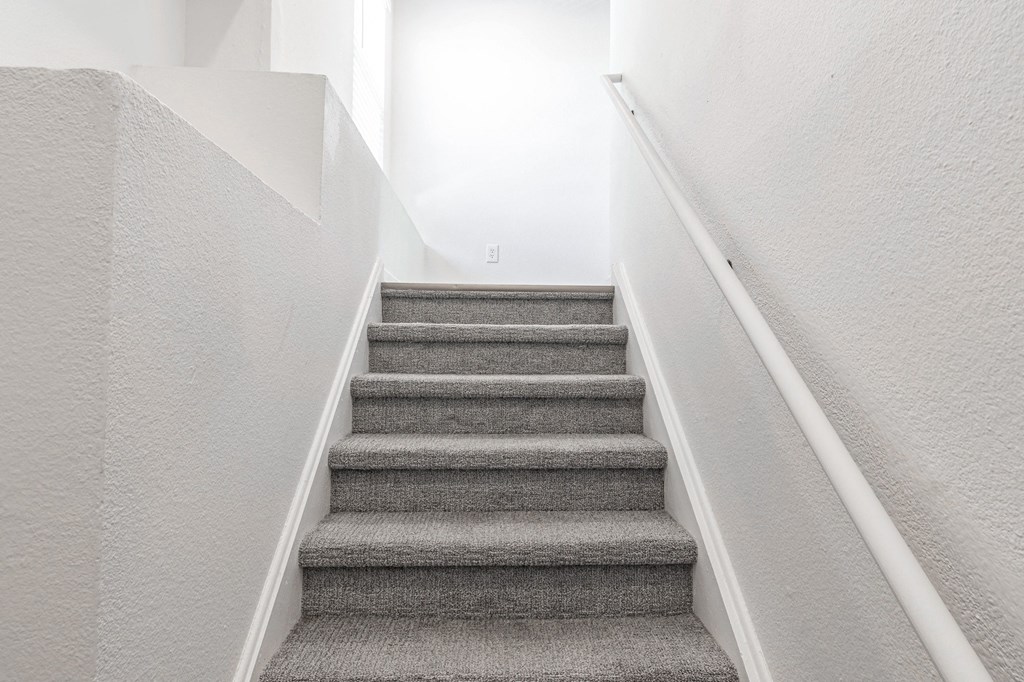 a staircase with grey carpeting and white walls and a white railing with a white at Latitudes Apartments, Indiana, 46237