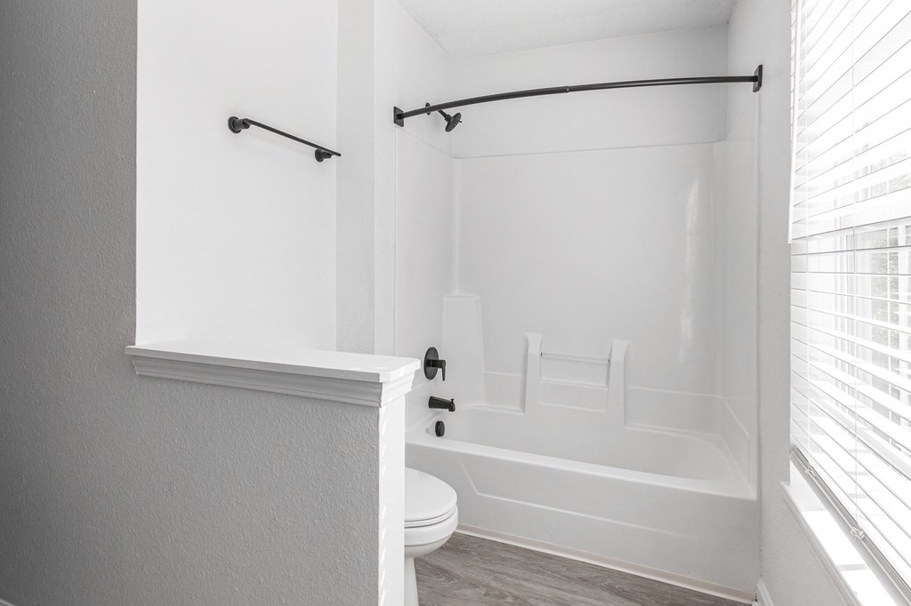 a white bathroom with a tub and a toilet and a window at Latitudes Apartments, Indianapolis, IN, 46237