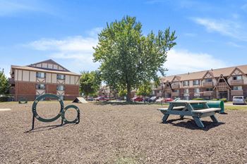 A playground with a green bench and a tree in the foreground and apartment buildings in the background.