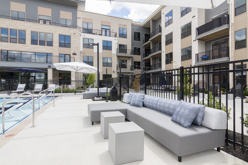 an outdoor lounge area with couches and tables in front of an apartment building