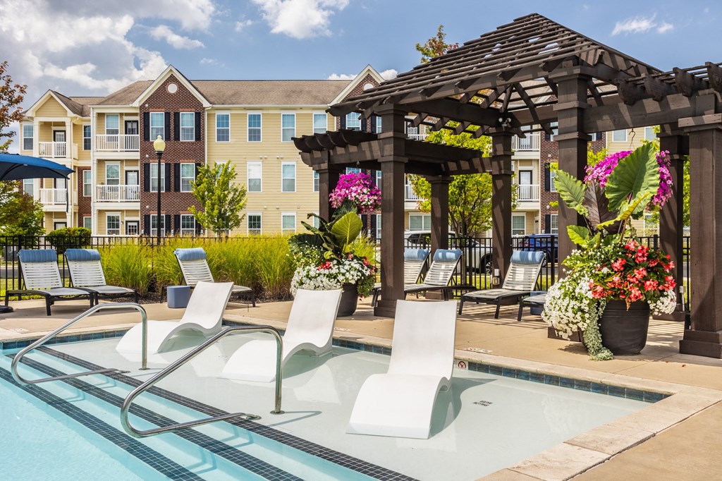 a swimming pool with lounge chairs and a gazebo with an apartment building at The Avenue at Polaris Apartments, Columbus, OH