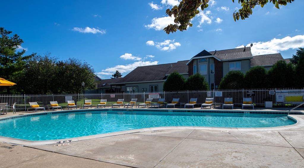 a swimming pool with lounge chairs and umbrellas in front of a building at Mallard Bay Apartments, Indiana