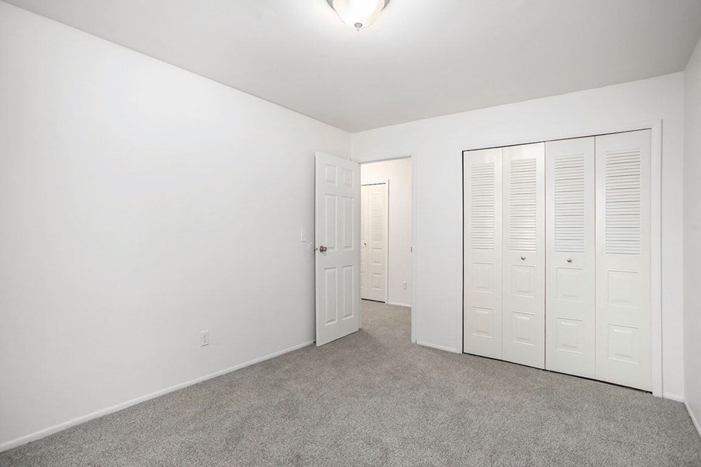 an empty bedroom with white closets and carpeting at Fairlane Apartments in Springfield, MI