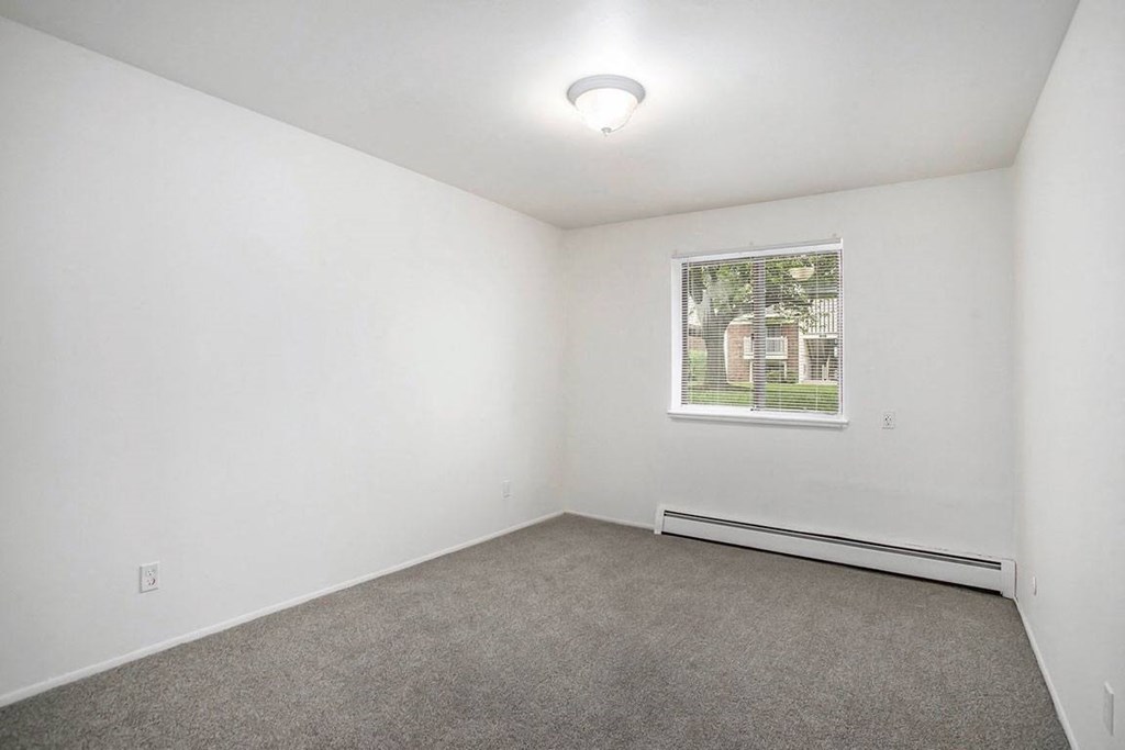 Large bedroom with carpet and a window at Fairlane Apartments in Springfield, MI