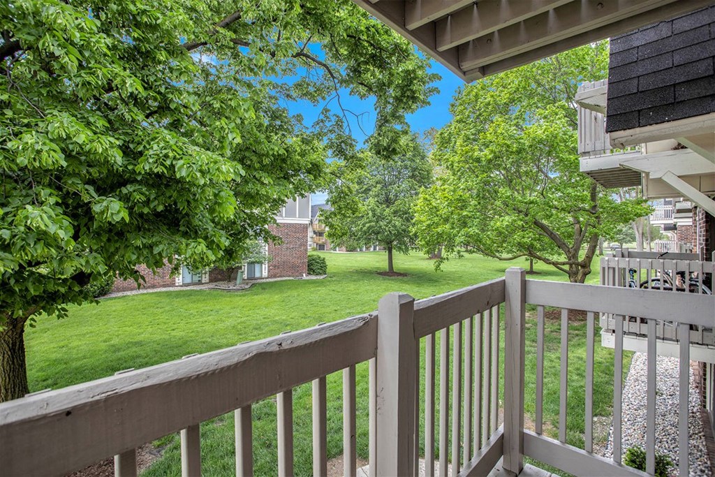 the view from a private balcony with mature shade trees at Fairlane Apartments in Springfield, MI