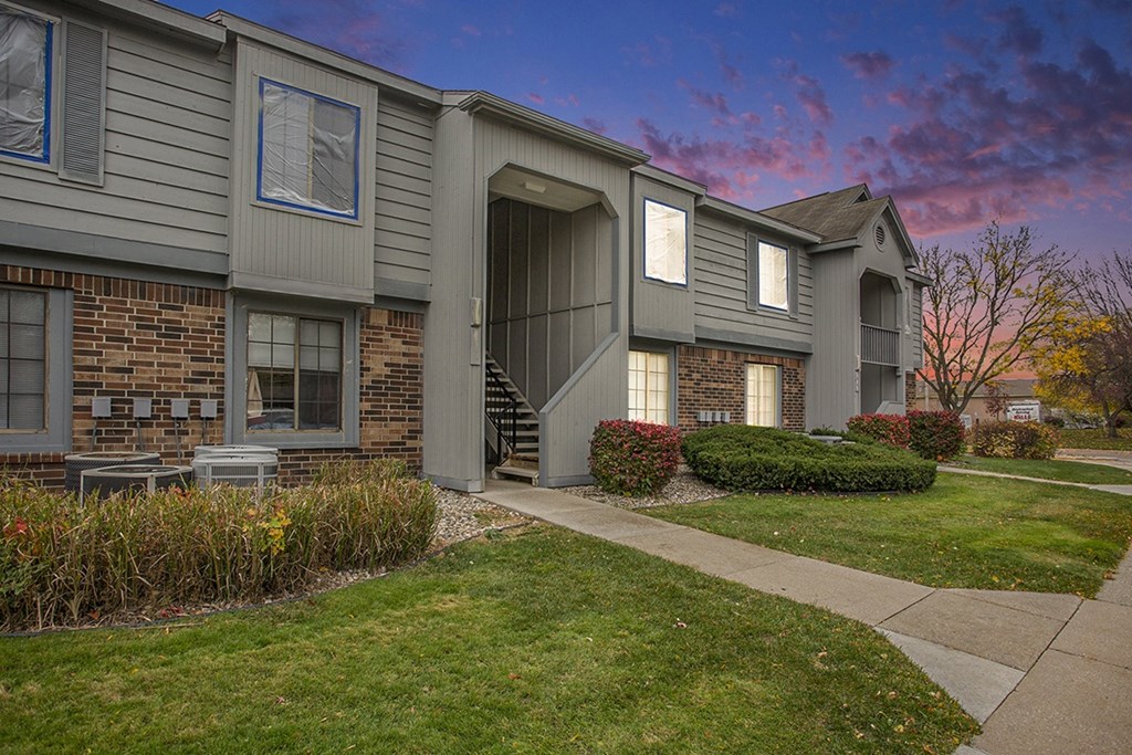 A grey building with a brick wall and landscaping in front at Hampton Lakes Apartments, Walker, 49534