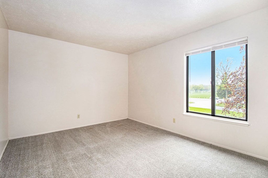 a bedroom with a large window and a carpeted floor at Hickory Village Apartments, Mishawaka, Indiana