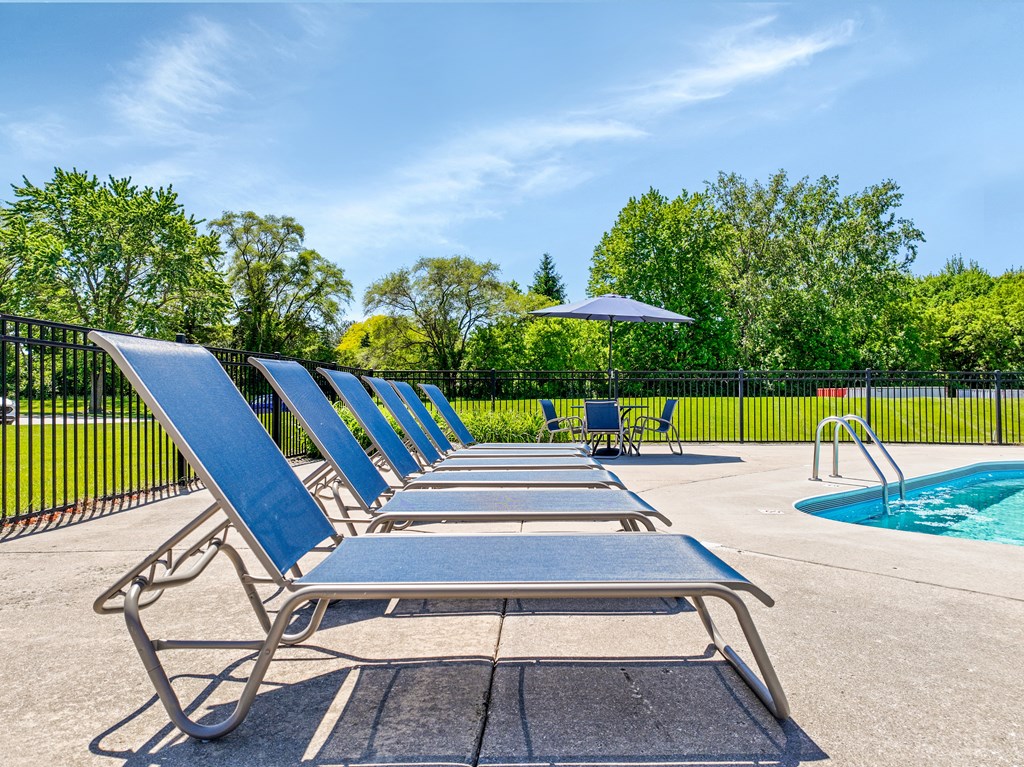 A row of sun loungers are set up by a pool.