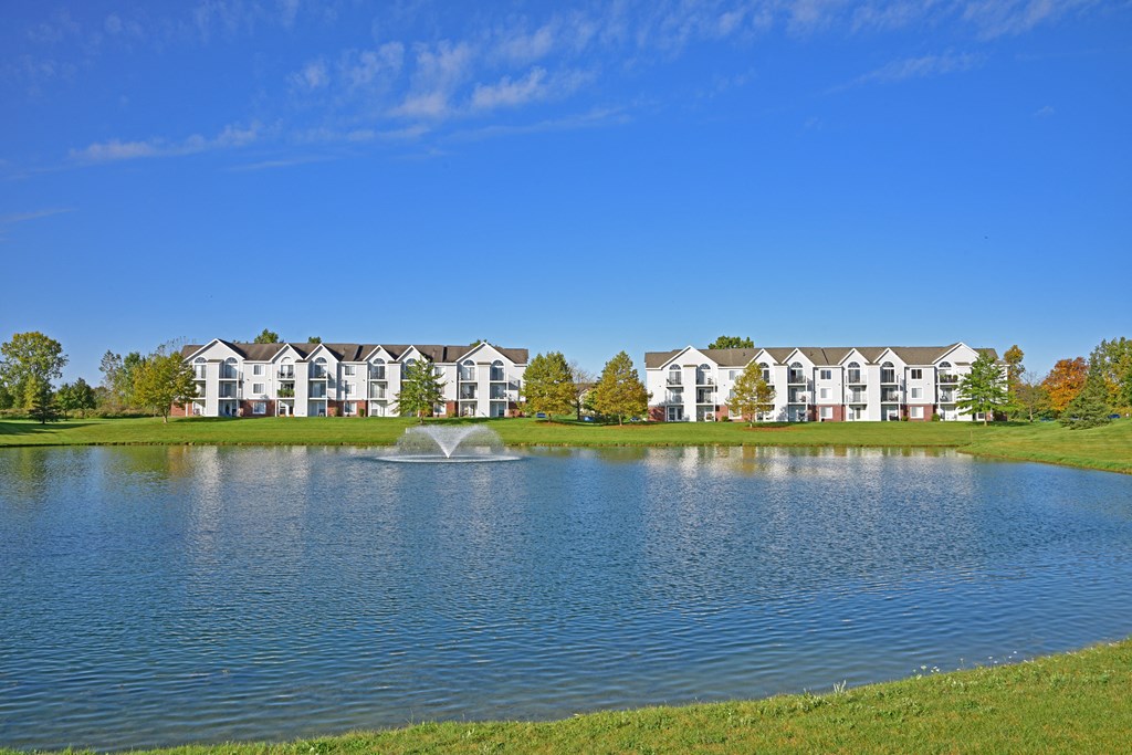 a lake with a fountain in front of a building at Heatherwood Apartments, Grand Blanc