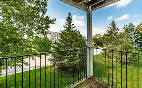 A balcony with a black railing and a view of a tree and a building in the background