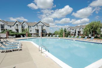 A large swimming pool with lounge chairs and apartment buildings in the background.