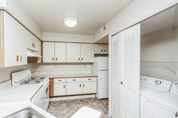 A small white kitchen with wooden cabinets and a stove top oven.