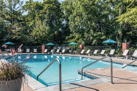 a swimming pool with chairs and trees in the background at Polo Run Apartments, Greenwood, IN