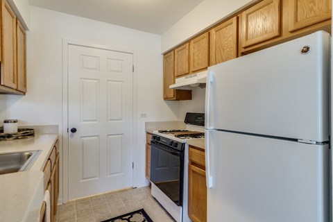 A white refrigerator stands in a kitchen with wooden cabinets and a white door.