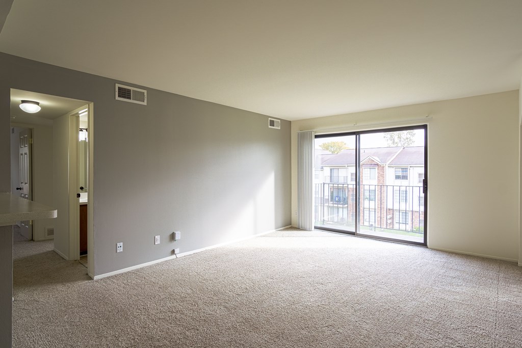 A large empty room with a carpeted floor and a sliding glass door leading to a balcony.