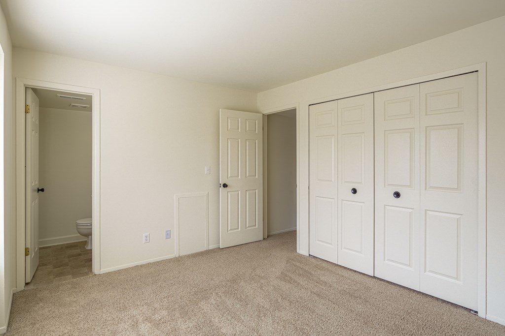 A room with white walls and carpeted floor with two doors.
