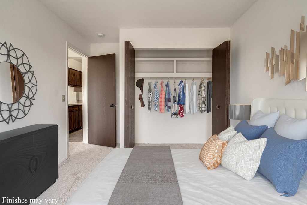 a bedroom with a large bed and a closet with clothes hanging on the wall at The Landings Apartments, Westland, MI