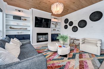 A living room with a grey couch, a white armchair, a white coffee table, a fireplace, and a wooden ceiling at Ironwood Flats Apartments, Brandon