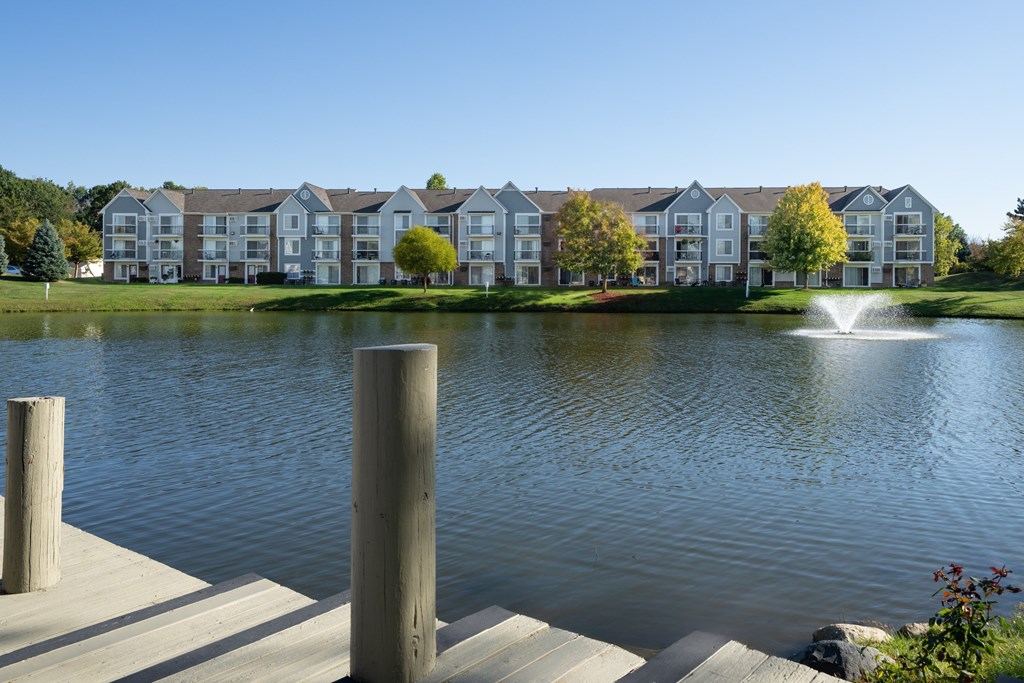 A lake in front of apartment buildings with a fountain in the middle.