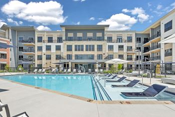 A large swimming pool surrounded by sun loungers in front of apartment buildings at Luxe 360 on Centerpointe Apartments, Virginia