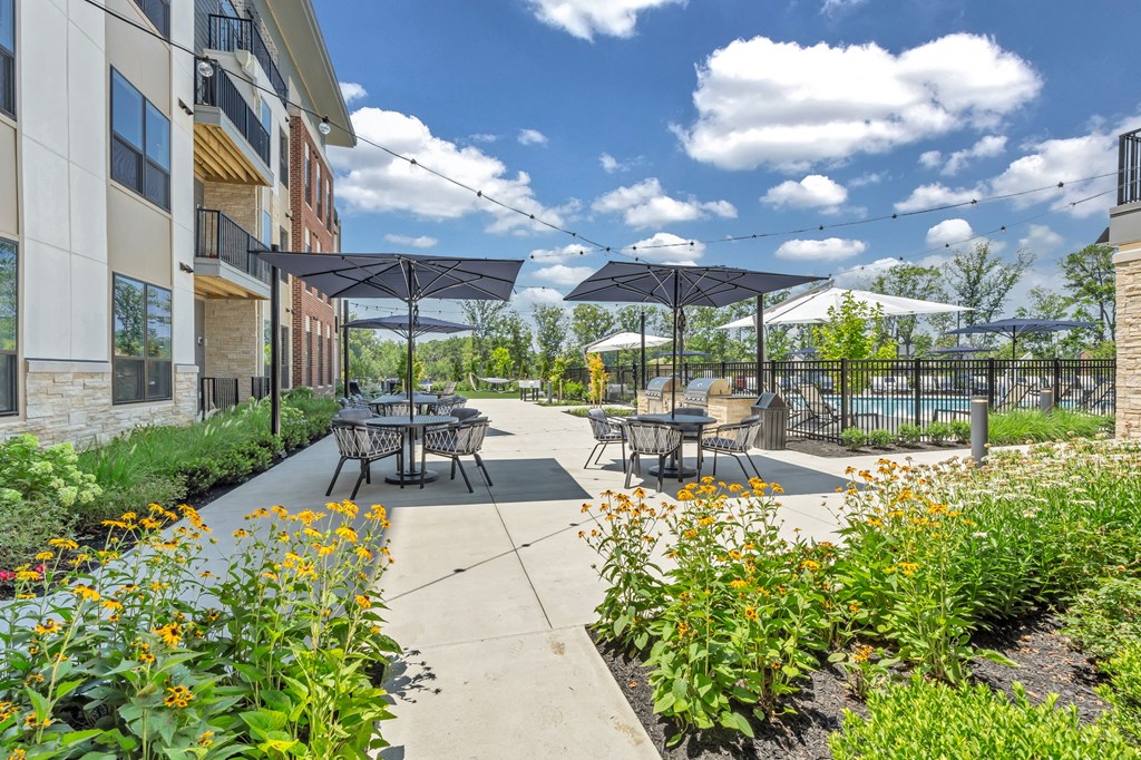 A patio with tables and chairs is surrounded by plants and flowers at Luxe 360 on Centerpointe Apartments, Midlothian, Virginia