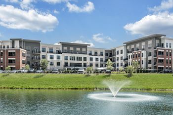 A fountain in the middle of a pond in front of apartment buildings