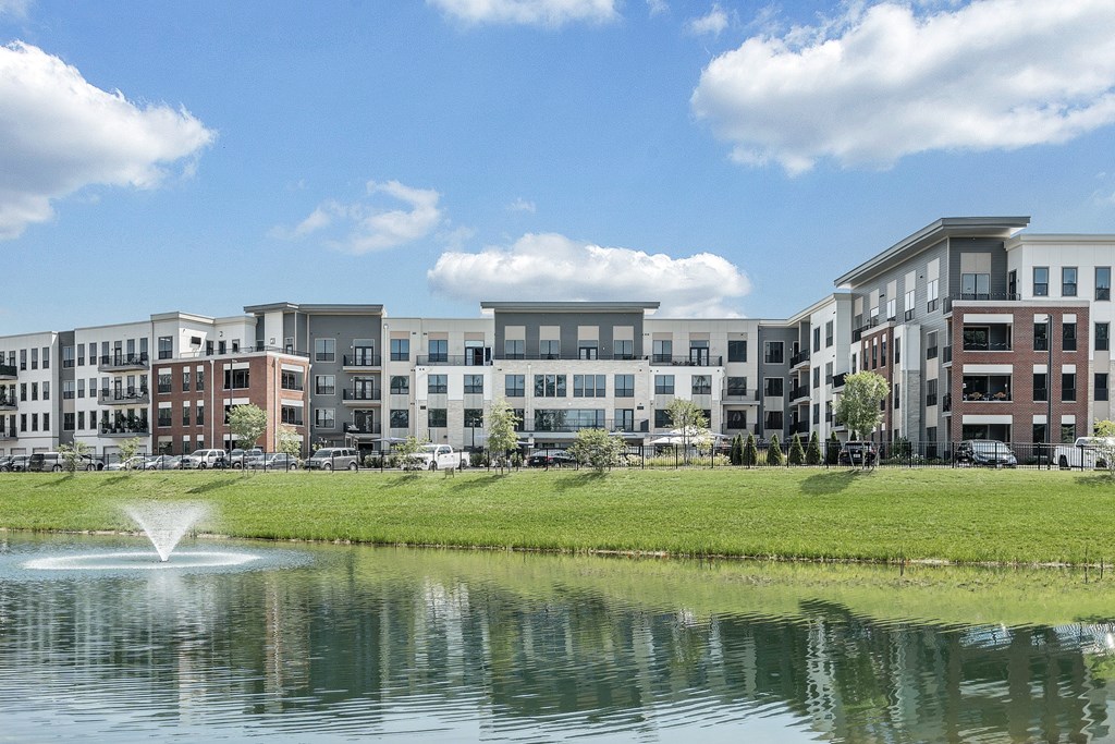 A fountain in front of a building with a blue sky and clouds in the background.