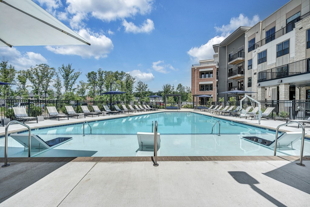 A large swimming pool surrounded by lounge chairs and trees.