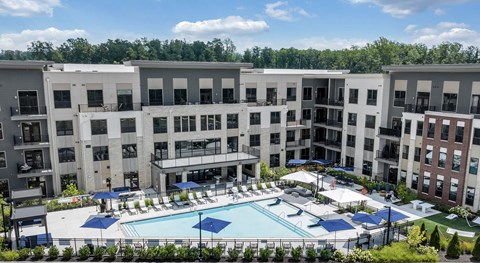 A large swimming pool surrounded by a fence and umbrellas in front of apartment buildings at Luxe 360 Apartment Complex in Midlothian Virginia
