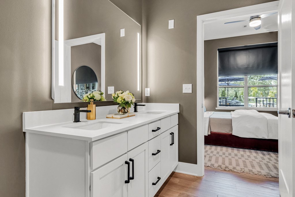 A bathroom with a vanity, mirror, and a bedroom in the background at Luxe 360 on Centerpointe Apartments, Virginia, 23114