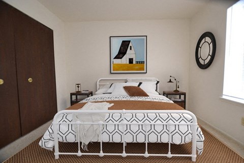 A bedroom with a white bed and a painting of a house above it.