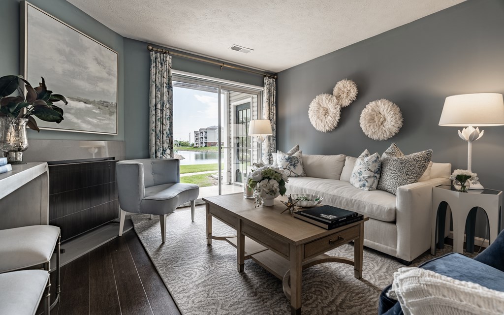 A living room with a white couch, a wooden coffee table, and a large window with a view of the outside at Mallard Bay Apartments, Crown Point, Indiana