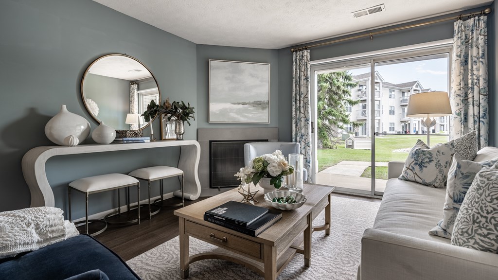 A living room with a sofa, a coffee table, a mirror, and a window with a view of a building at Mallard Bay Apartments, Crown Point, Indiana