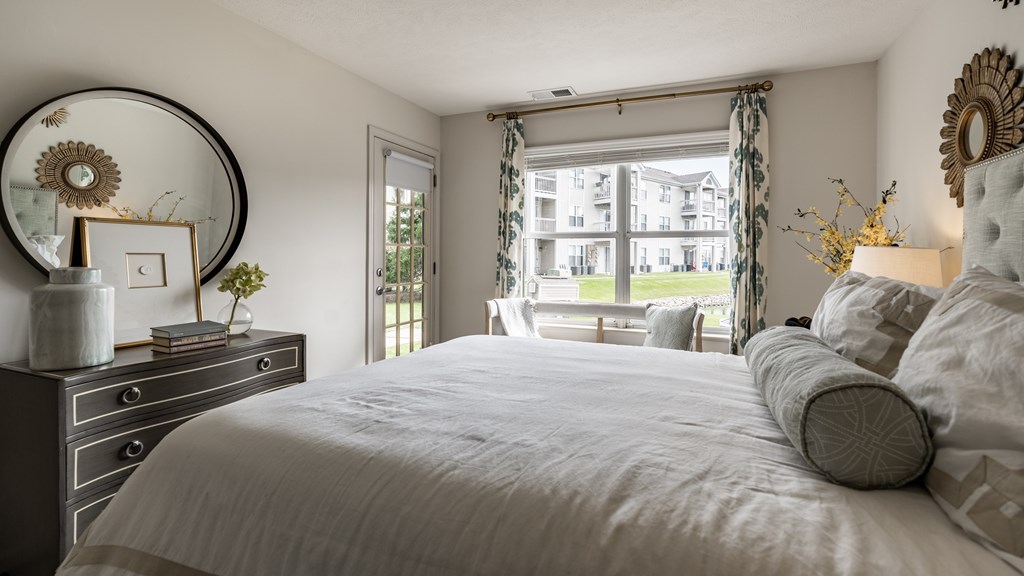 A bedroom with a large bed, a dresser, and a window with curtains at Mallard Bay Apartments, Crown Point, Indiana