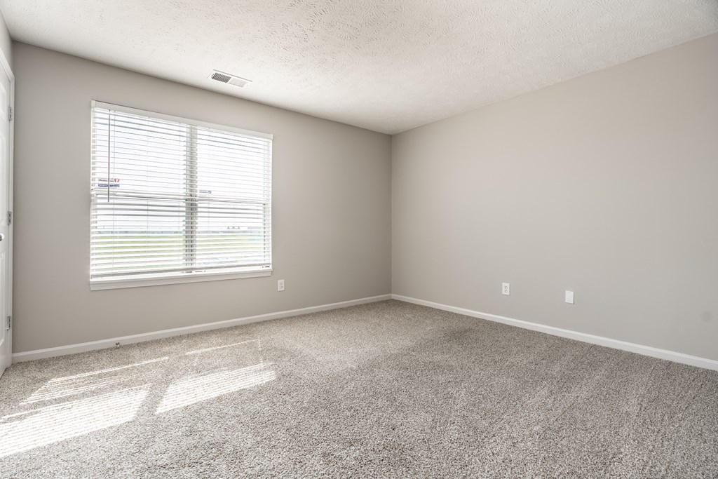 A room with a carpeted floor and a window with blinds at Mallard Bay Apartments, Crown Point, Indiana