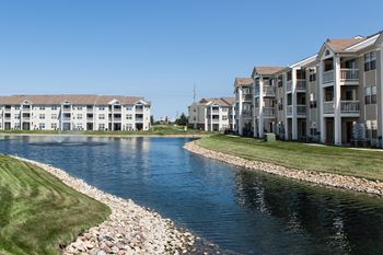 A river runs through a grassy area next to apartment buildings at Mallard Bay Apartments, Indiana