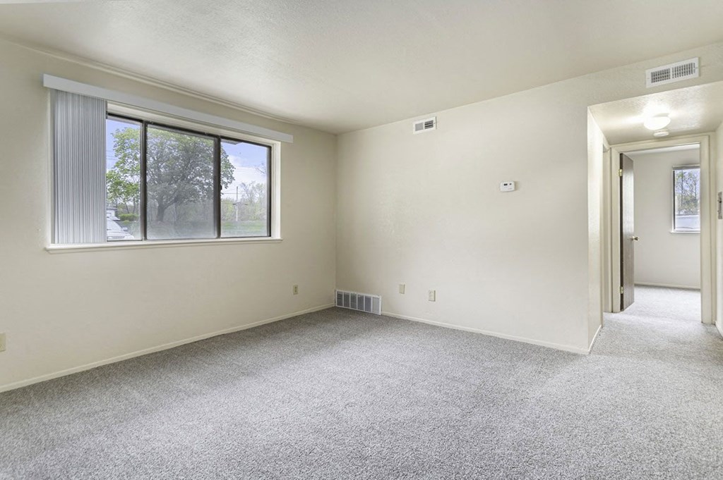 an empty living room with a large window and carpeting at Normandy Village Apartments, Michigan City, IN