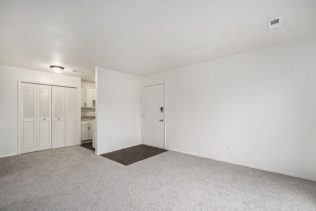 an empty living room and kitchen with white walls and carpet at Normandy Village Apartments, Indiana