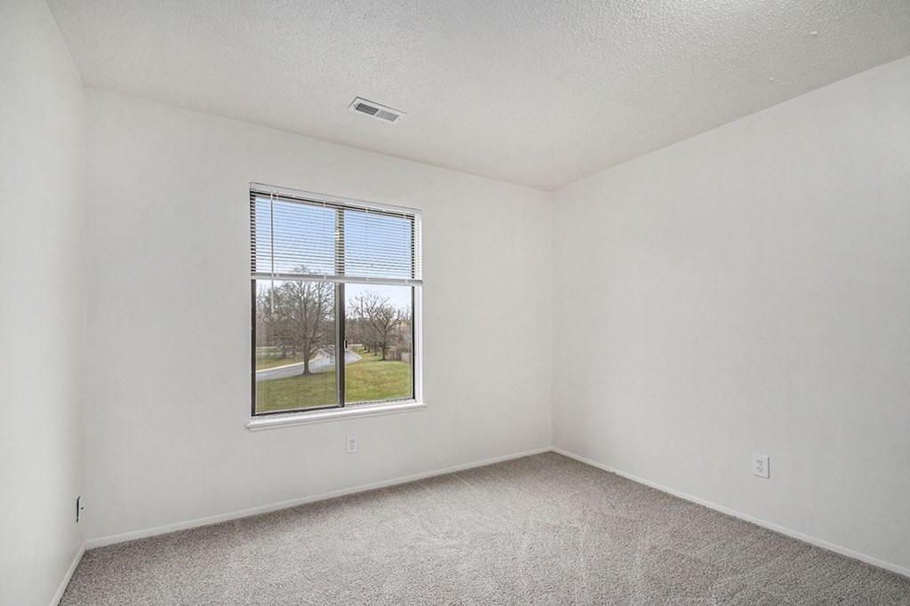 an empty bedroom with a window and carpeted floor at Normandy Village Apartments, Michigan City, Indiana