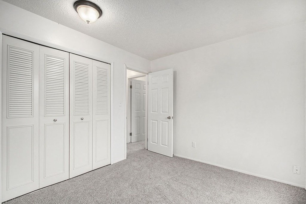 an empty bedroom with white closet doors at Normandy Village Apartments, Michigan City