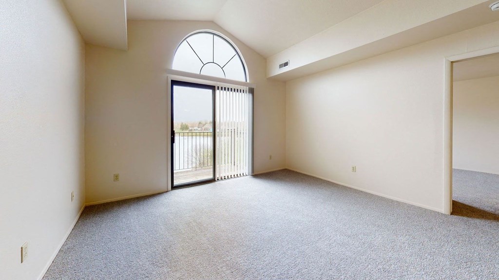 an empty living room with a cathedral ceiling and a glass door to a balcony