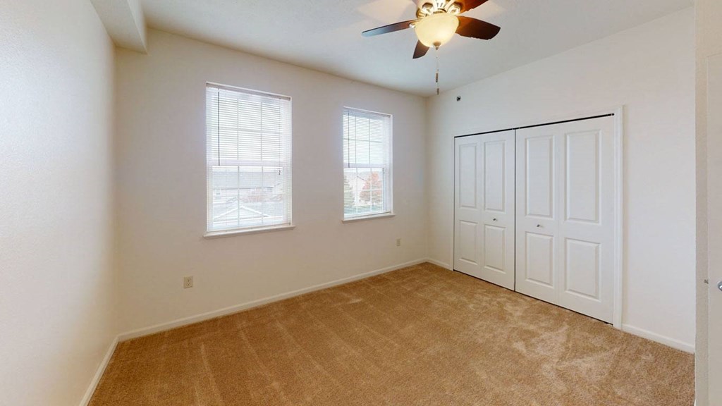 an empty bedroom with a ceiling fan and two windows  at Hunters Pond Apartment Homes, Champaign