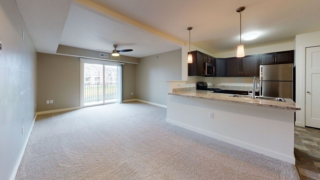 A spacious living room and a kitchen with a breakfast bar at The Reserve at Destination Pointe apartments, Grimes, IA