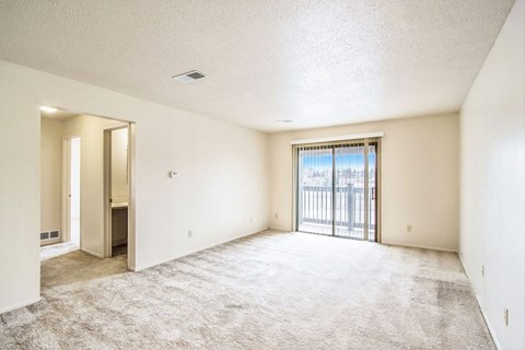 A spacious living room with a carpeted floor and a sliding glass door leading to a balcony at Seville Apartments, Kalamazoo, MI
