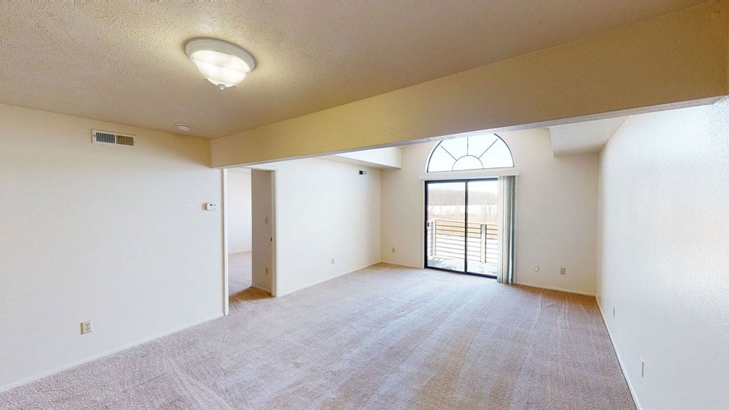 spacious living room with a cathedral ceiling and a door to a balcony at South Bridge Apartments in Fort Wayne, Indiana