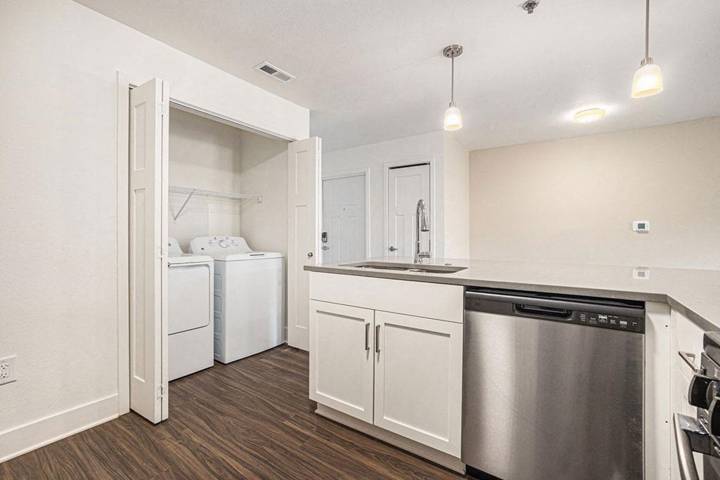 a white kitchen with a stainless steel dishwasher and a washer/dryer at Stoney Pointe Apartment Homes, Kansas