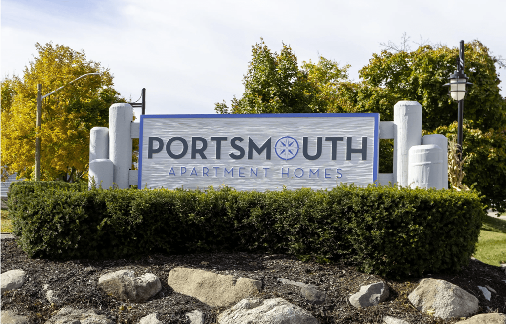 A sign for Portsmouth Apartment Homes is displayed in front of a hedge.